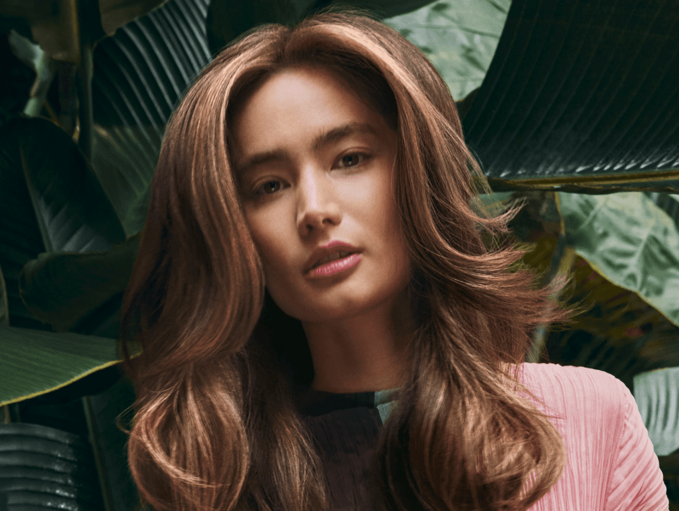 Woman with soft, flowing balayage colour in a lush green setting — representing expertly blended Aveda colour at The Pamper Suite in Bexley.