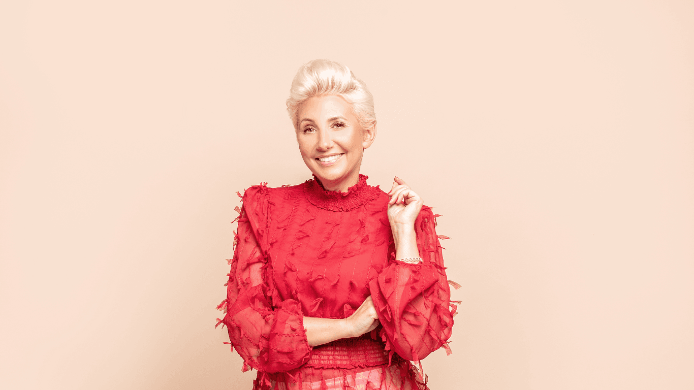 Smiling woman with platinum blonde styled hair wearing a red textured blouse, representing a professional cut and finish result at The Pamper Suite in Bexley.