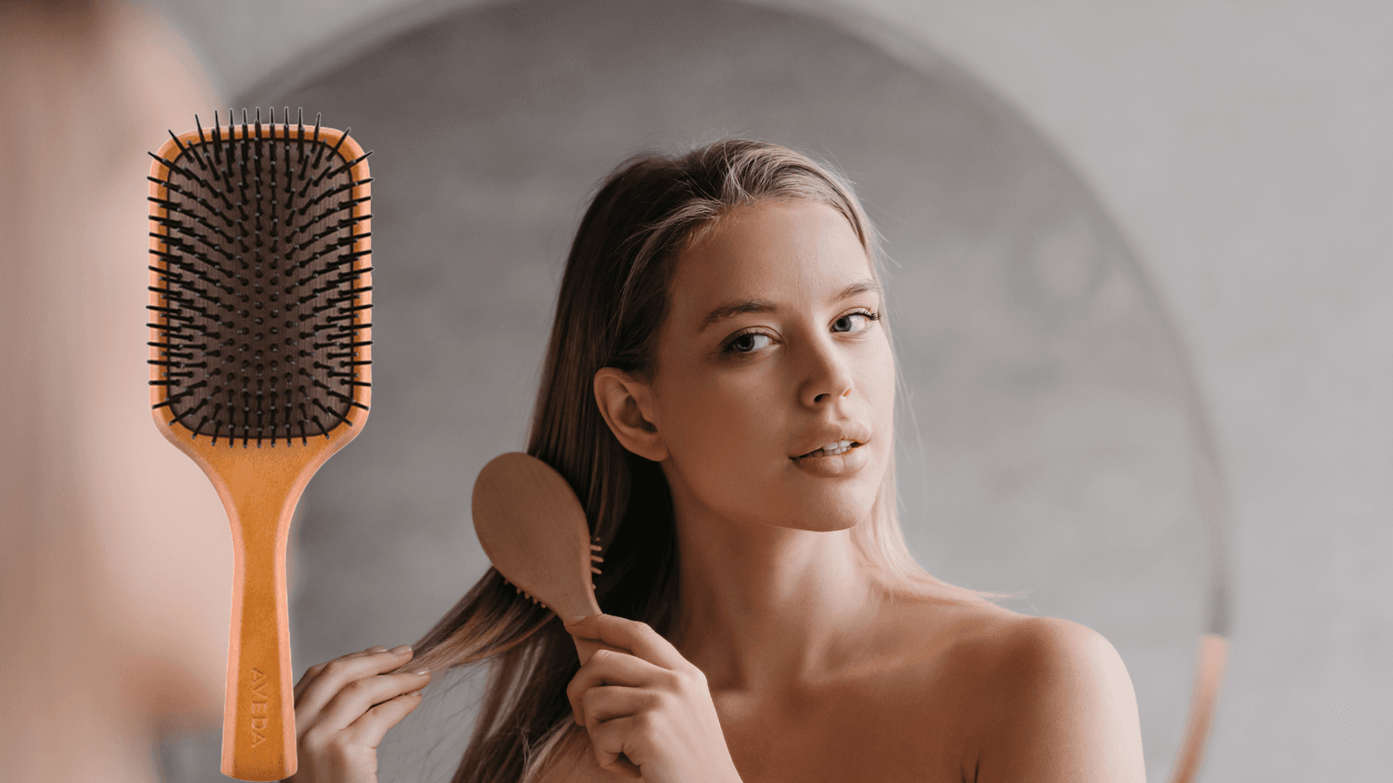 A woman brushing her hair beside a close-up of the Aveda Paddle Brush – featured as a free gift with Pamper Suite Mother’s Day gift cards in Bexley.