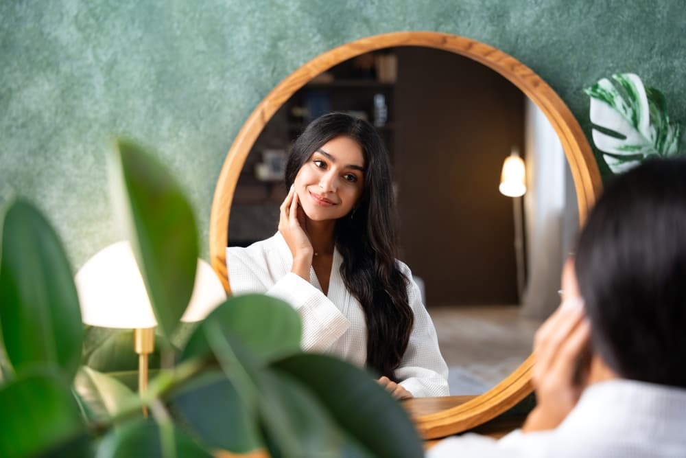 Woman with long dark hair admiring her reflection in a round mirror after a professional hair treatment at The Pamper Suite in Bexley.