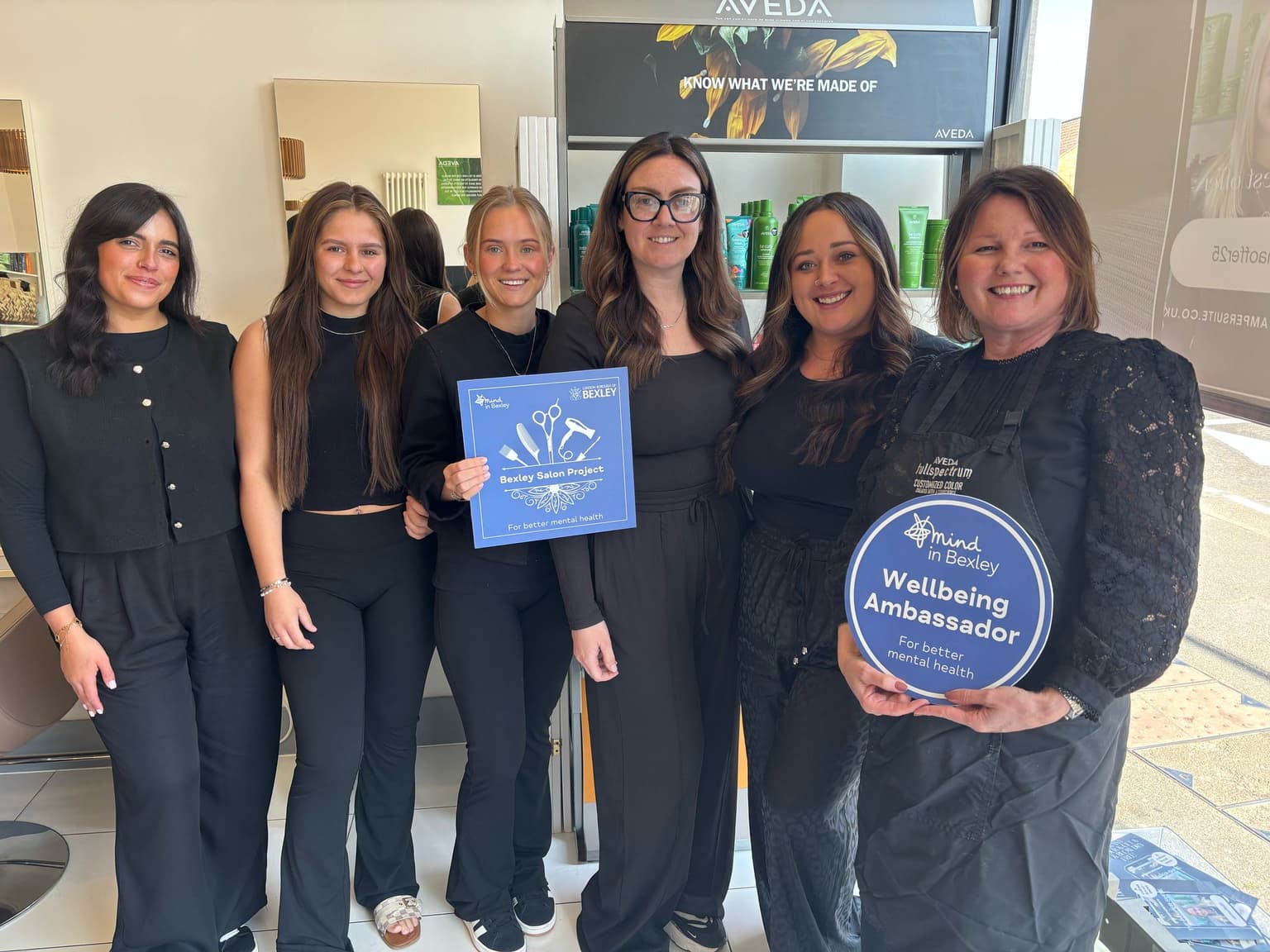 The Pamper Suite team in Bexley, pictured in salon holding ‘Wellbeing Ambassador’ and ‘Bexley Salon Project’ signs, supporting better mental health.