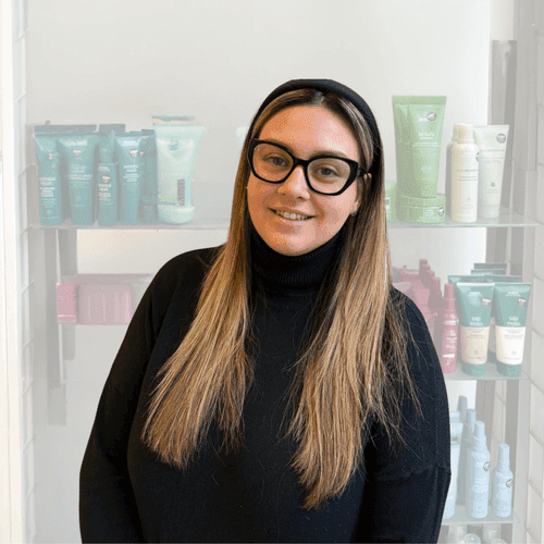 Sara White, experienced hair stylist at The Pamper Suite in Bexley, standing in front of Aveda product shelves.